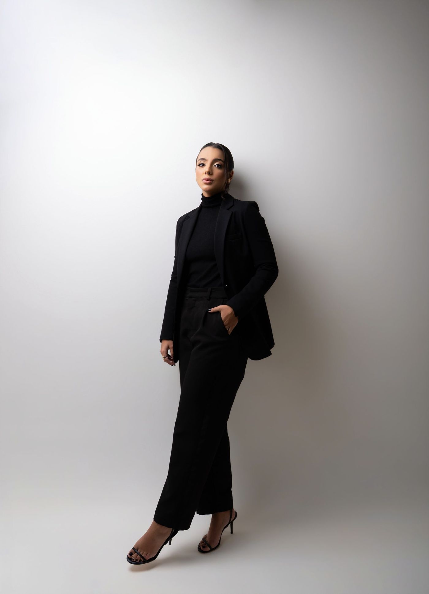 Laura Mendonça Jayme, de terno preto, em pé diante de um fundo claro